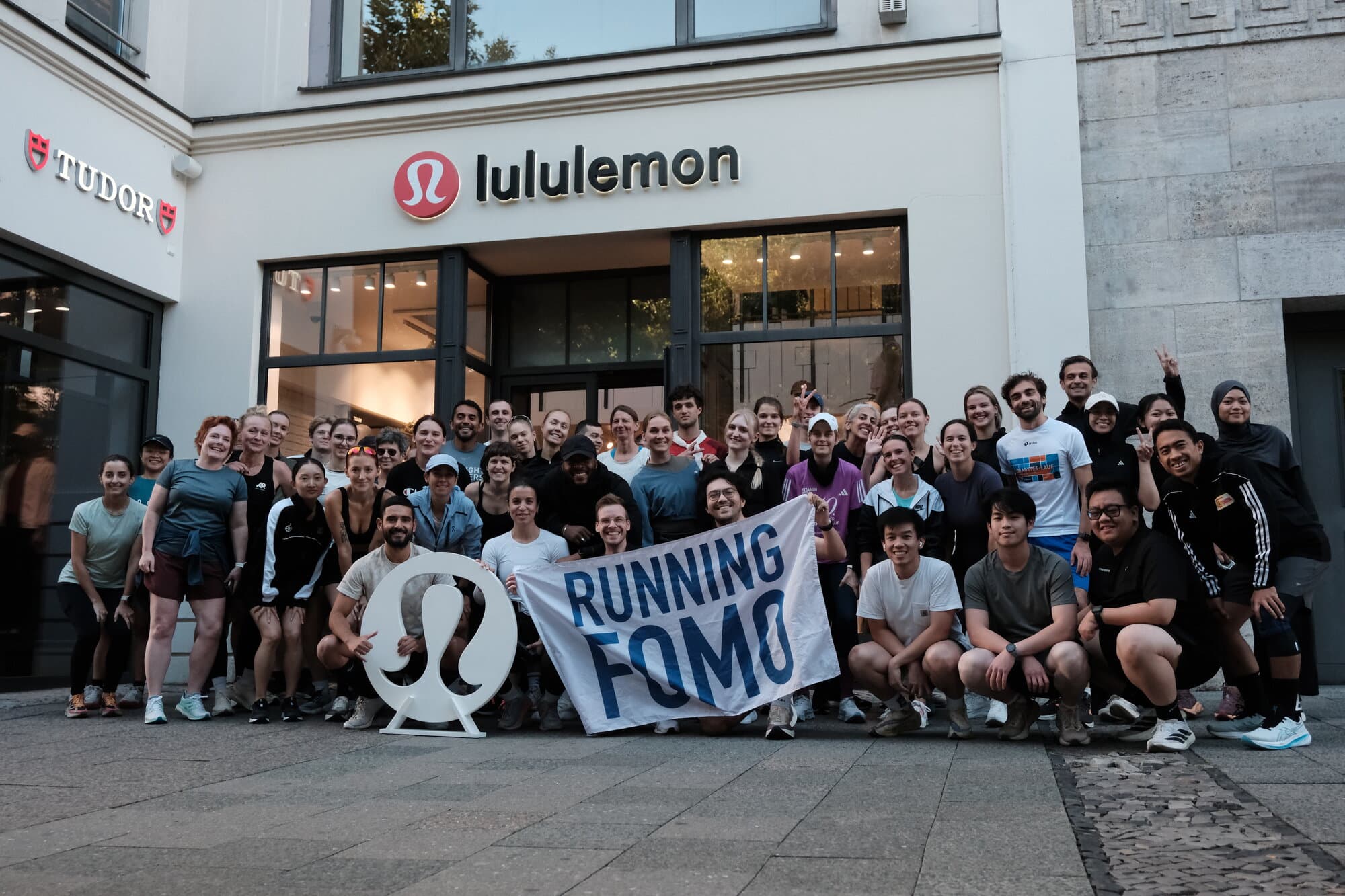 A group of people poses outside a Lululemon store holding a Running FOMO banner.