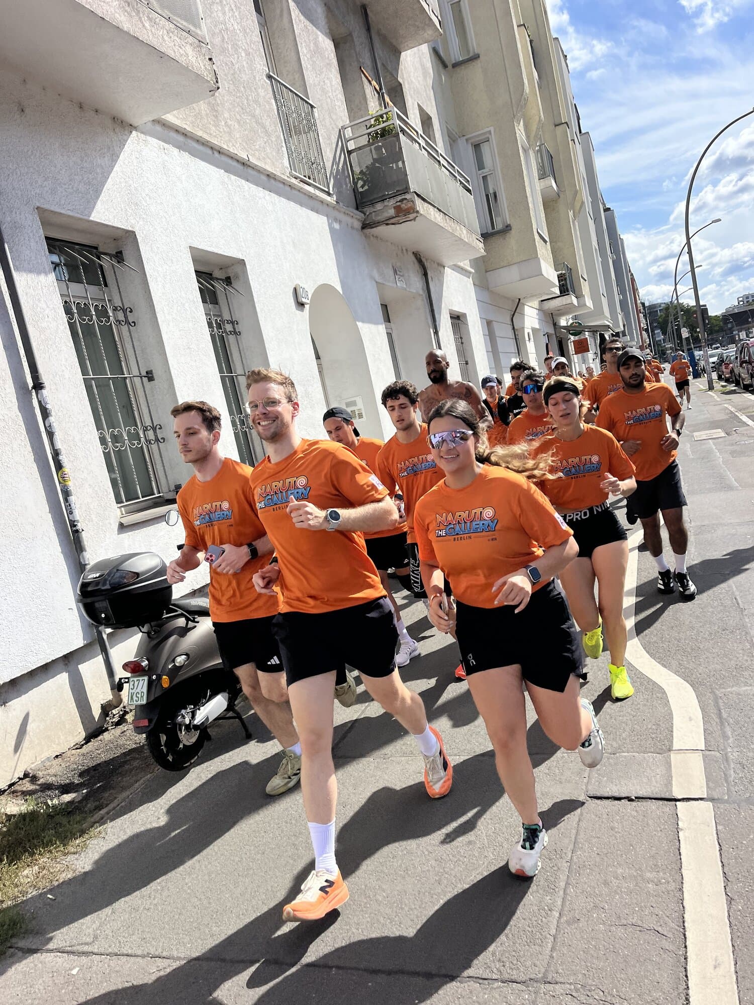 A group of people in matching shirts run together on a sunny street.