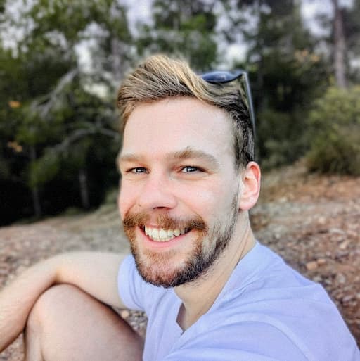 A man smiling outdoors with trees in the background.